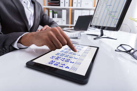 Close-up Of A Businessperson's Hand Using Calendar On Digital Tablet At Workplaceの写真素材