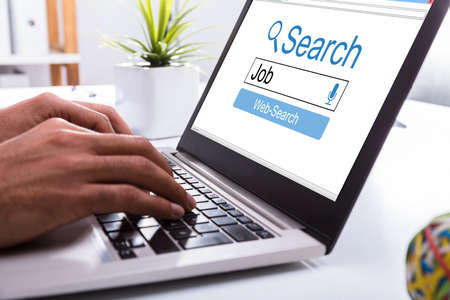 Close-up Of A Businessperson's Hand Searching Online Job On Laptop At Workplaceの写真素材