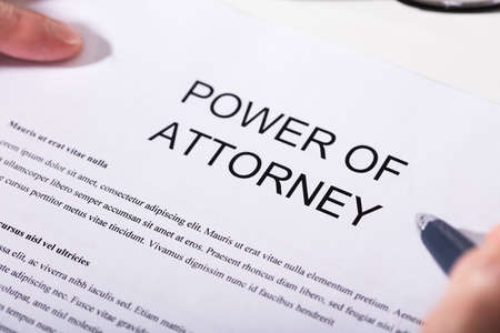 Close-up Of A Person Holding Pen Over Power Of Attorney Formの写真素材
