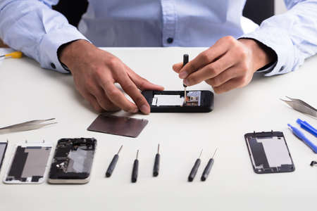 Close-up Of A Technician's Hand Repairing Mobile Phone On Deskの写真素材