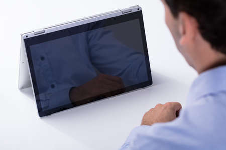 Rear View Of A Man Looking At Blank Hybrid Laptop Over The White Deskの写真素材