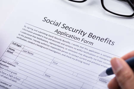 Close-up Of A Person's Hand Filling Social Security Benefits Application Formの写真素材