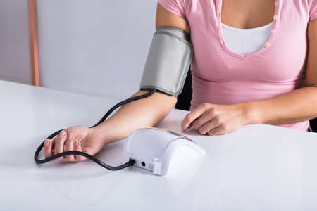 Midsection Of A Woman Measuring Her Blood Pressure On Table
