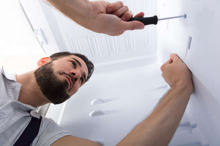 Close-up Of A Male Electrician Fixing Refrigerator In Kitchenの写真素材