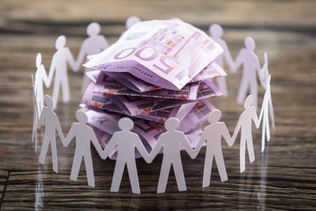 Close-up Of Paper Cut Out Human Figure Surrounding Stacked Banknotes On Deskの写真素材