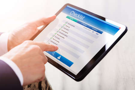 Close-up Of A Businessperson's Hand Filling Checklist Form On Digital Tabletの写真素材