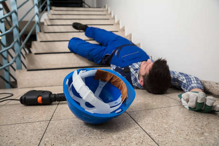 Unconscious Handyman Lying On Staircase With Helmet And Drill On Floorの写真素材