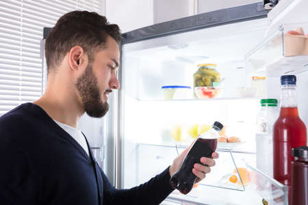 Close-up Of A Young Man Holding Drink Bottle Near Open Refrigeratorの写真素材