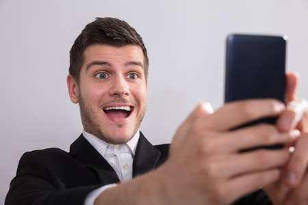 Close-up of a happy young businessman looking at smartphoneの写真素材