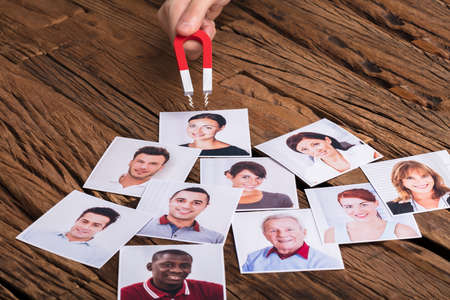 Close-up Of A Businessperson's Hand With Horseshoe Magnet Attracting Photograph Of Smiling Peopleの写真素材