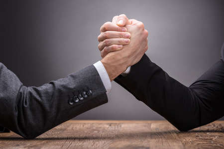 Close-up Of Two Businesspeople Competing In Arm Wrestling On Grey Background