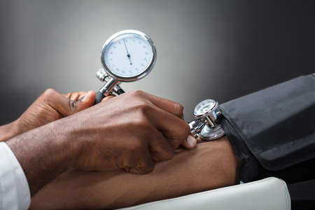 Close-up Of Male Doctor Measuring The Blood Pressure Of Patient Against Gray Background
