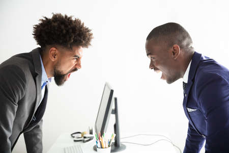 Two Angry Young Businessmen Shouting At Each Other At Workplaceの写真素材