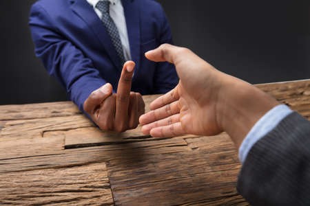 Close-up Of Businessman's Hand Showing Middle Finger To His Partnerの写真素材