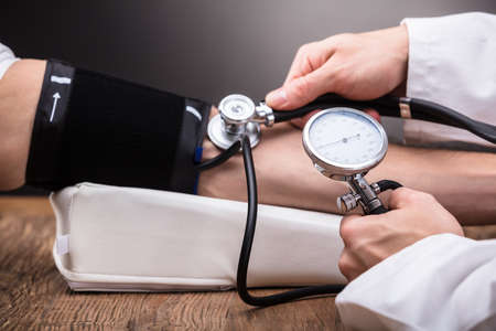 Close-up Of Doctor's Hand Checking Patient's Blood Pressure Over Wooden Table