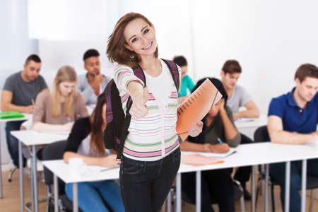 Portrait Of A Smiling Female Student Holding Books In Classroomの写真素材