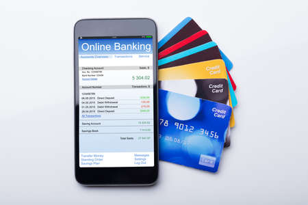 High Angle View Of Mobilephone With Online Banking App And Credit Card On White Background