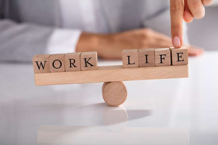 Close-up Of Businessperson's Finger Showing Imbalance Between Work And Life On Wooden Seesawの写真素材