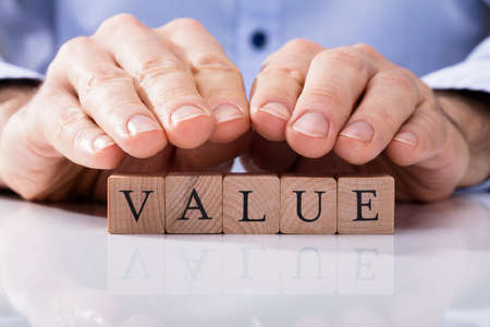 Close-up Of Human Hand Over Wooden Block With Value Text On Deskの写真素材