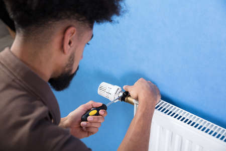 Close-up Of A Young Male Plumber Installing Radiator With Screwdriverの写真素材