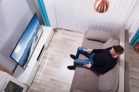 High Angle View Of A Young Man Holding Remote Watching Television At Homeの写真素材