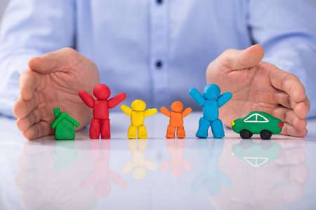 Close-up Of Man's Hand Protecting The House, Car And Colorful Family Made Up Of Clayの写真素材