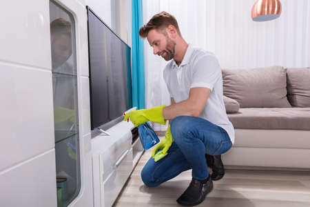 Young Man Wearing Gloves Cleaning Furniture With Spray Bottle