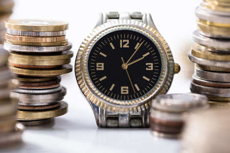 Wrist Watch Surrounded With The Stack Of Coins On The White Deskの写真素材