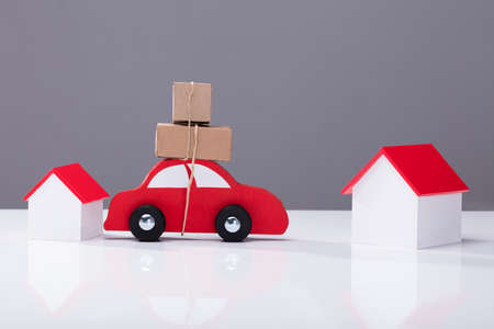 Red Car Transporting Cardboard Boxes From One House To Another On White Deskの写真素材