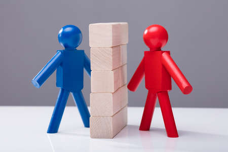 Red And Blue Human Figures Separated By Wooden Blocks Against Grey Background