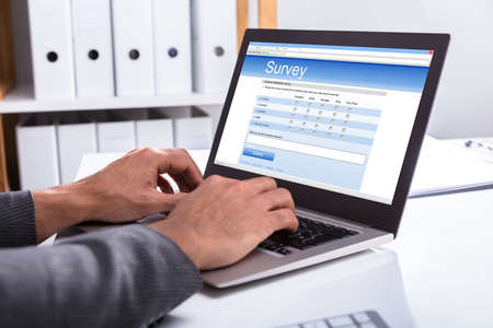 Close-up Of A Businessperson's Hand Filling Online Survey Form On Laptop In Office