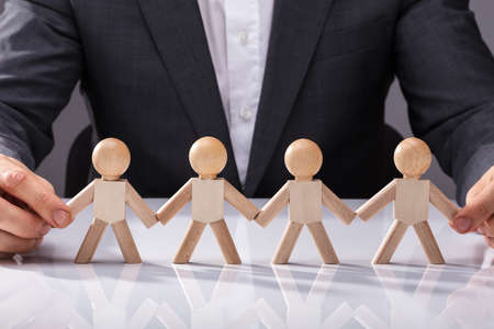 Close-up Of A Person's Holding Hand Of Wooden Figures On White Deskの写真素材