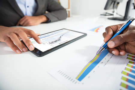 Two Businesspeople Using Digital Tablet While Analyzing Graph In Office
