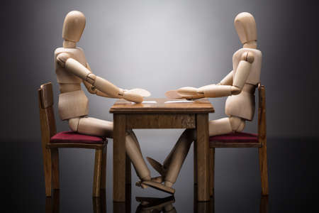 Elevated View Of Two Wooden Dummy Figures Discussing Business Document At Workplaceの写真素材