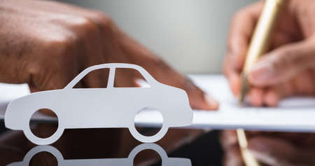 A Person's Hand Signing Car Loan Agreement Contract With Car Silhouette On Glass Deskの写真素材