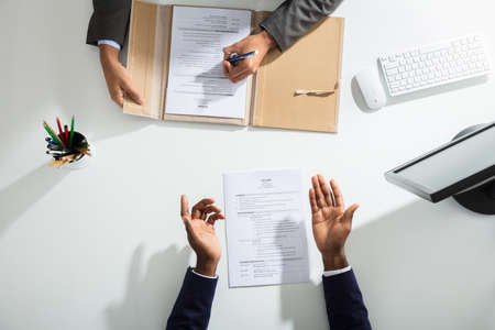 Elevated View Of Businessperson And Candidates Hand With Resume On White Deskの素材 [FY31094067685]