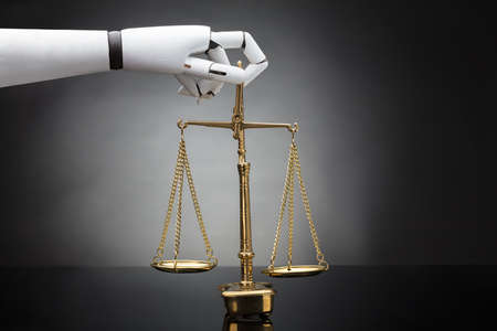 Close-up Of A Robot's Hand Holding Justice Scale On Grey Backgroundの写真素材