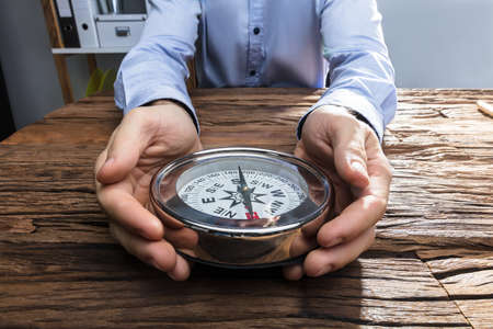 Close-up Of A Businessperson's Hand Holding Compass On Wooden Desk