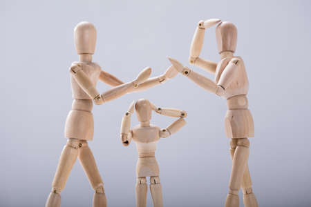 Child Dummy Suffering From Quarrels Between Wooden Figure Parents Against White Background
