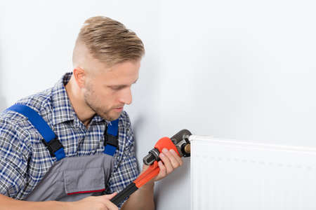 Close-up Of Male Plumber Fixing Thermostat Using Wrench At Homeの写真素材