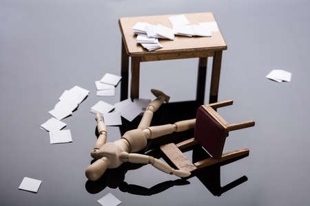 Unconscious Wooden Dummy Figure Lying On Floor With Scattered Documents At Workplace