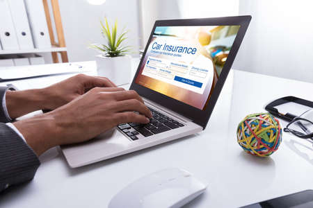 Close-up Of A Businessperson's Hand Filling Car Insurance Form On Laptop In Officeの写真素材