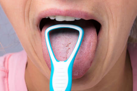 Close-up Of Young Woman Cleaning Tongue With Cleanerの写真素材