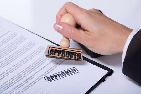 Close-up Of Person Hands Using Stamper On Document With The Text Approved