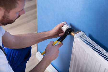 Close-up Of A Young Male Repairman Fixing Radiator With Wrench