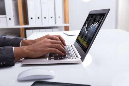 Close-up Of A Businessperson's Hand Analyzing Financial Graph On Laptop At Workplace