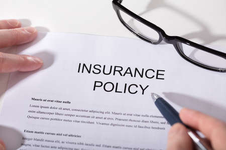 Close-up Of A Person's Hand Holding Pen Over Insurance Policy Form