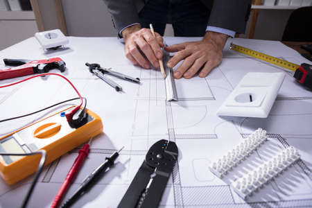 Architect Using Pencil To Draw Blueprint Besides Tools And Digital Multimeter