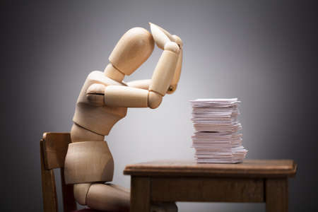 Wooden Dummy Figure Suffering From Headache Sitting On Chair With Stack Of Documents On Deskの写真素材