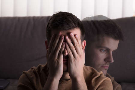 Young Sad Man Sitting In Front Of Sofa At Home
